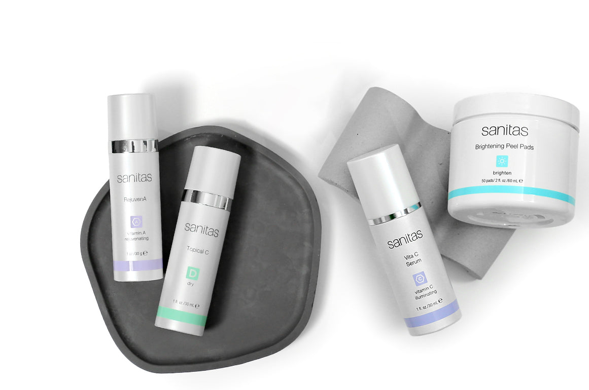 A set of Sanitas skincare products arranged on a white background, including a dark gray tray & light gray stone piece.