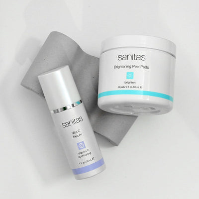 Sanitas skincare products including a vita c serum and brightening peel pads on a light gray background